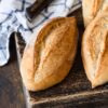 Einfache Dinkelbrötchen über Nacht auf einem rustikalen Holzbrett mit einem Tuch und Messer im Hintergrund.