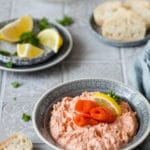 Lachscreme in einer Schüssel mit Räucherlachs und Zitronen im Hintergrund.