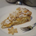 Ein Stück weihnachtliche Bratapfel-Tarte auf einem Teller mit einem Plätzchen und einer Gabel im Vordergrund.