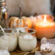 Weiße Schoko-Panna Cotta mit Likör auf einem Holzteller und Kürbissen sowie einer Kerze im Hintergrund.