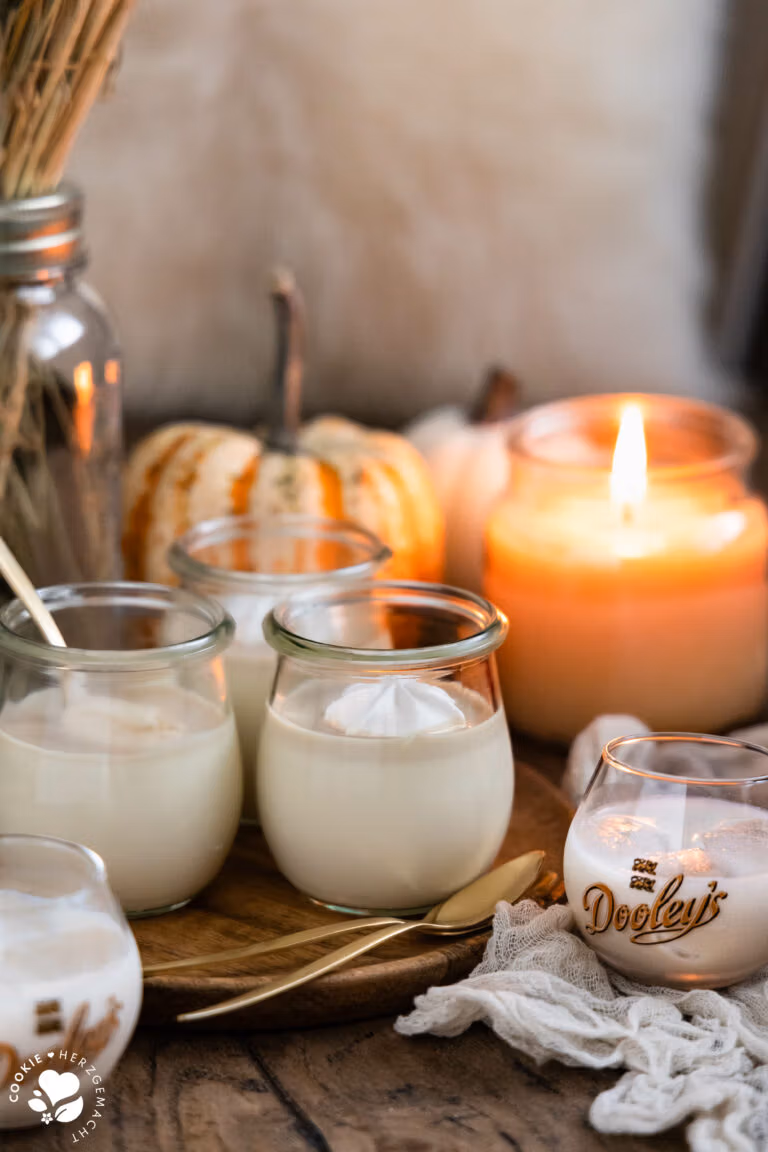Weiße Schoko-Panna Cotta mit Likör auf einem Holzteller und Kürbissen sowie einer Kerze im Hintergrund.
