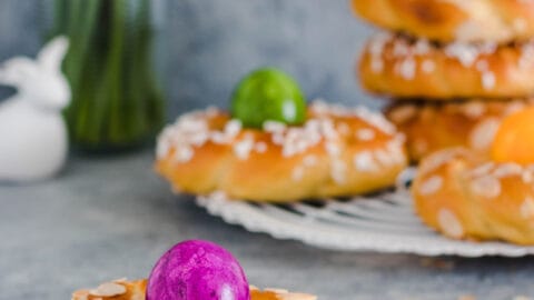 Osterkränze aus Dinkelmehl mit gefärbten Eiern und Narzissen im Hintergrund.