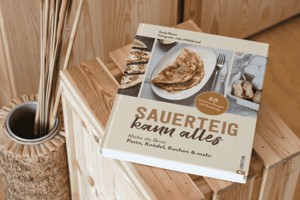 Backbuch und Kochbuch mit Sauerteig "Sauerteig kann alles" auf einem Holztisch