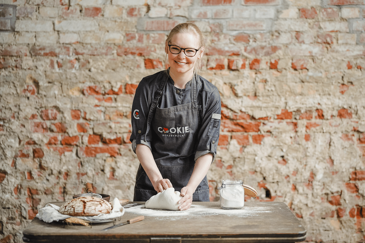 Sonja Bauer von Cookie und Co beim formen von Brotteig auf einem Holztisch vor einer Backsteinwand