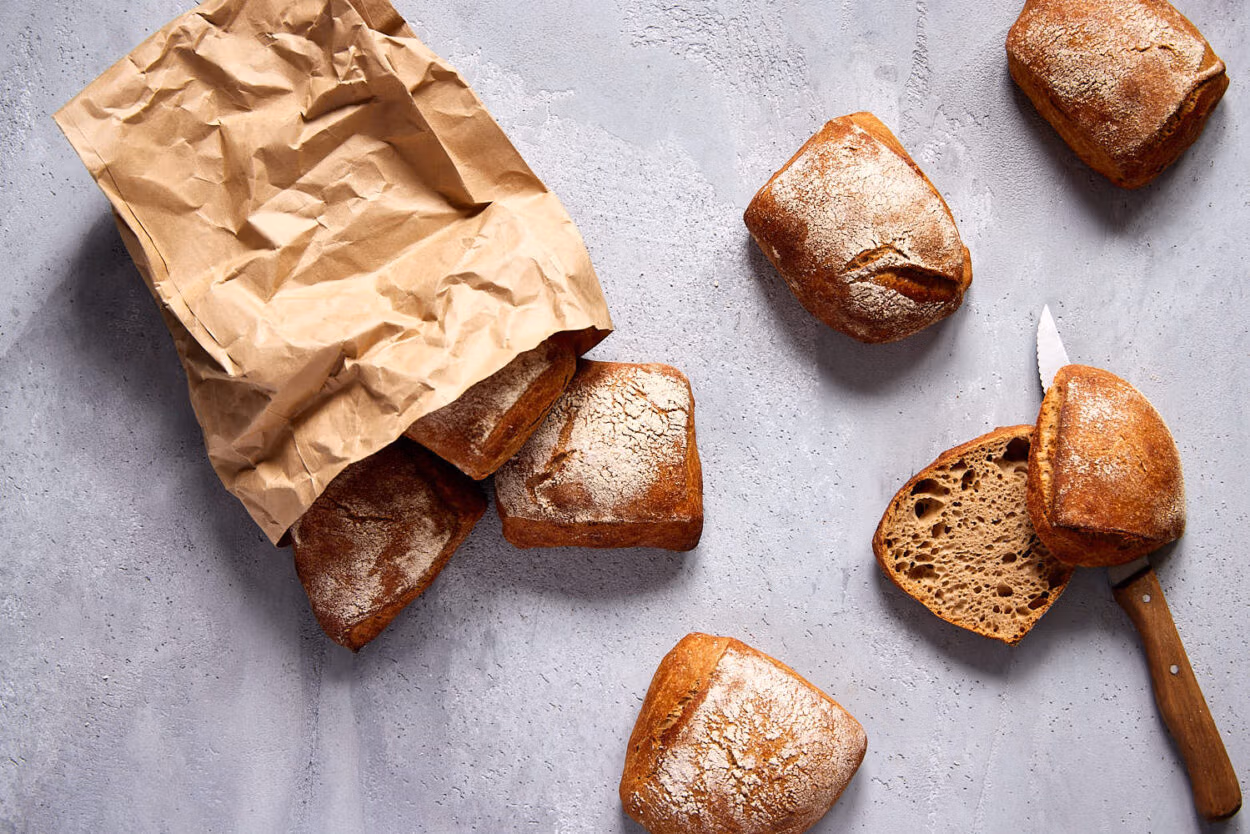 Nahaufnahme von knusprigen, aufgeschnittenen Vollkornbrötchen mit einem kleinen Brotmesser daneben.