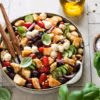 Italienischer Brotsalat „Panzanella“ in einer Salatschüssel mit einem Topf Basilikum im Vordergrund.