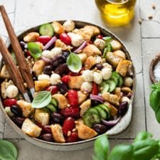 Italienischer Brotsalat „Panzanella“ in einer Salatschüssel mit einem Topf Basilikum im Vordergrund.