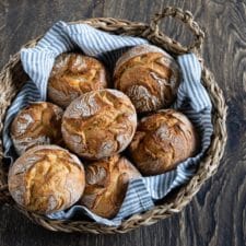 Rustikale Auffrischbrötchen mit Sauerteigresten in einem Brötchenkorb mit einem Blau gestreiften Tuch. Die Brötchen haben einer aromatische, lockere Krume und knusprige Kruste.