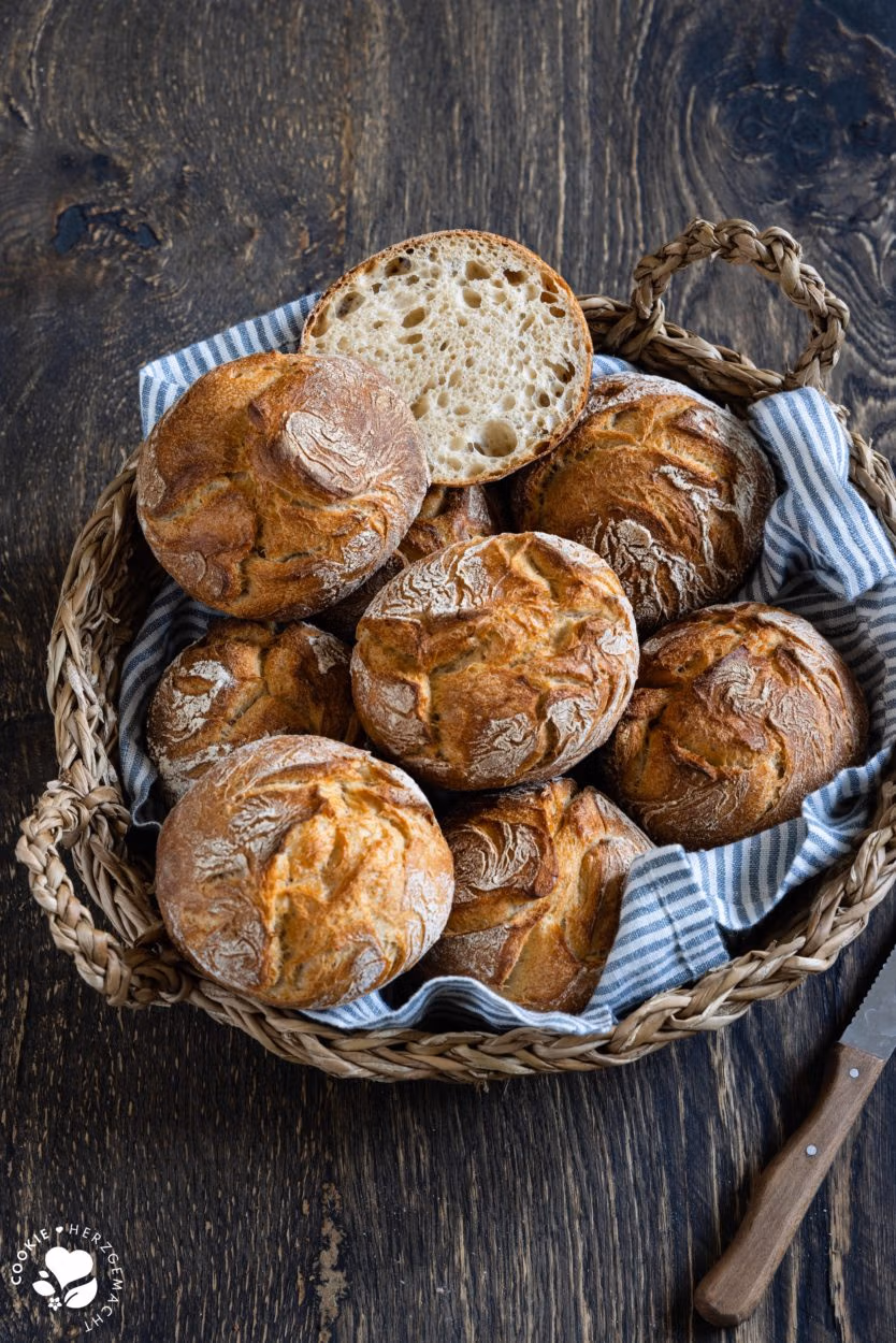 Rustikale Auffrischbrötchen mit Sauerteigresten in einem Brötchenkorb mit einem Blau gestreiften Tuch. Die Brötchen haben einer aromatische, lockere Krume und knusprige Kruste.