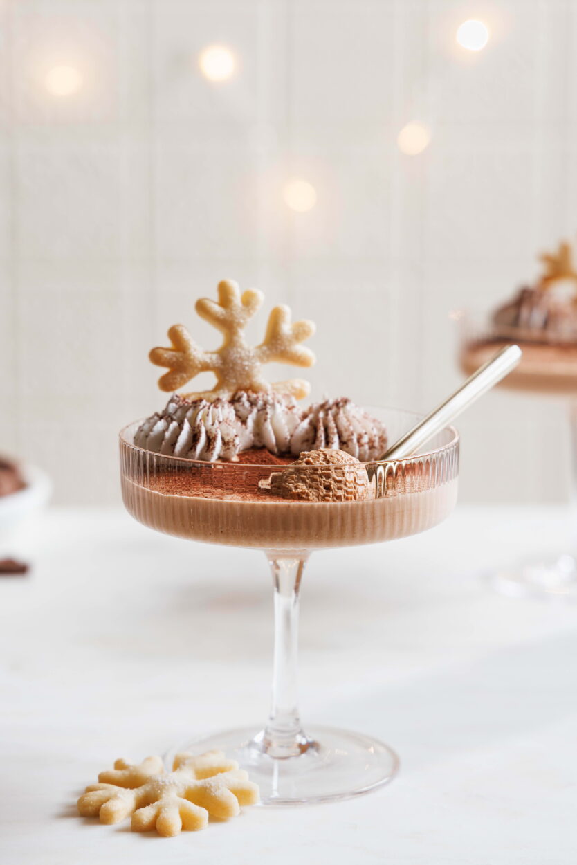 Schokomousse in einem Dessertglas mit Sahne, Kakao einem Plätzchen in Form einer Schneeflocke dekoriert. mit einem goldenen Löffel.