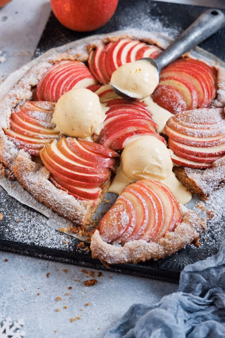 Eine Apfelgalette auf einem Backblech mit leinem Eisportioniere und leicht geschmolzenen Vanilleeiskugeln.