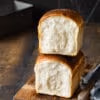 Ein aufgeschnittenes Toastbrot auf einem Holzbrett mit einem Messer und einer Backform im Hintergrund.