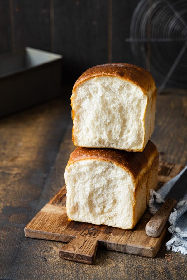 Ein aufgeschnittenes Toastbrot auf einem Holzbrett mit einem Messer und einer Backform im Hintergrund.