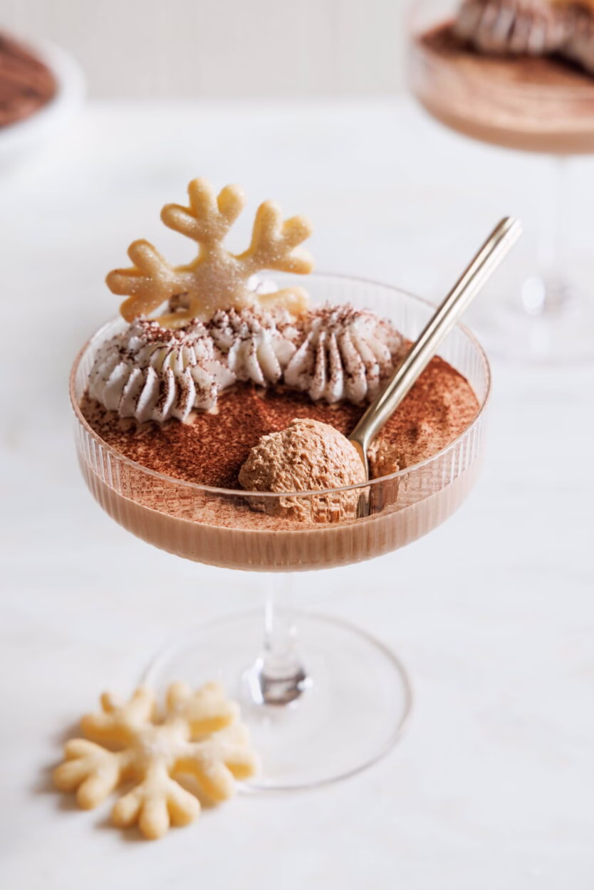 Baileysmousse in einem Champagnerglas, mit Sahne, Kakao und einem Plätzen n Schneeflockenform dekoriert.