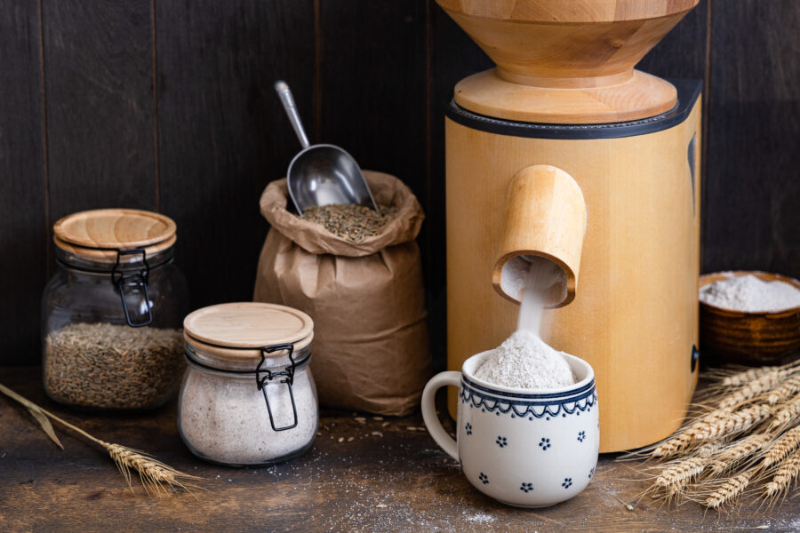 Eine Getreidemühle in der Mehl in eine Tasse gemachlen wird mit Ähren und, Mehl und Getreide daneben.