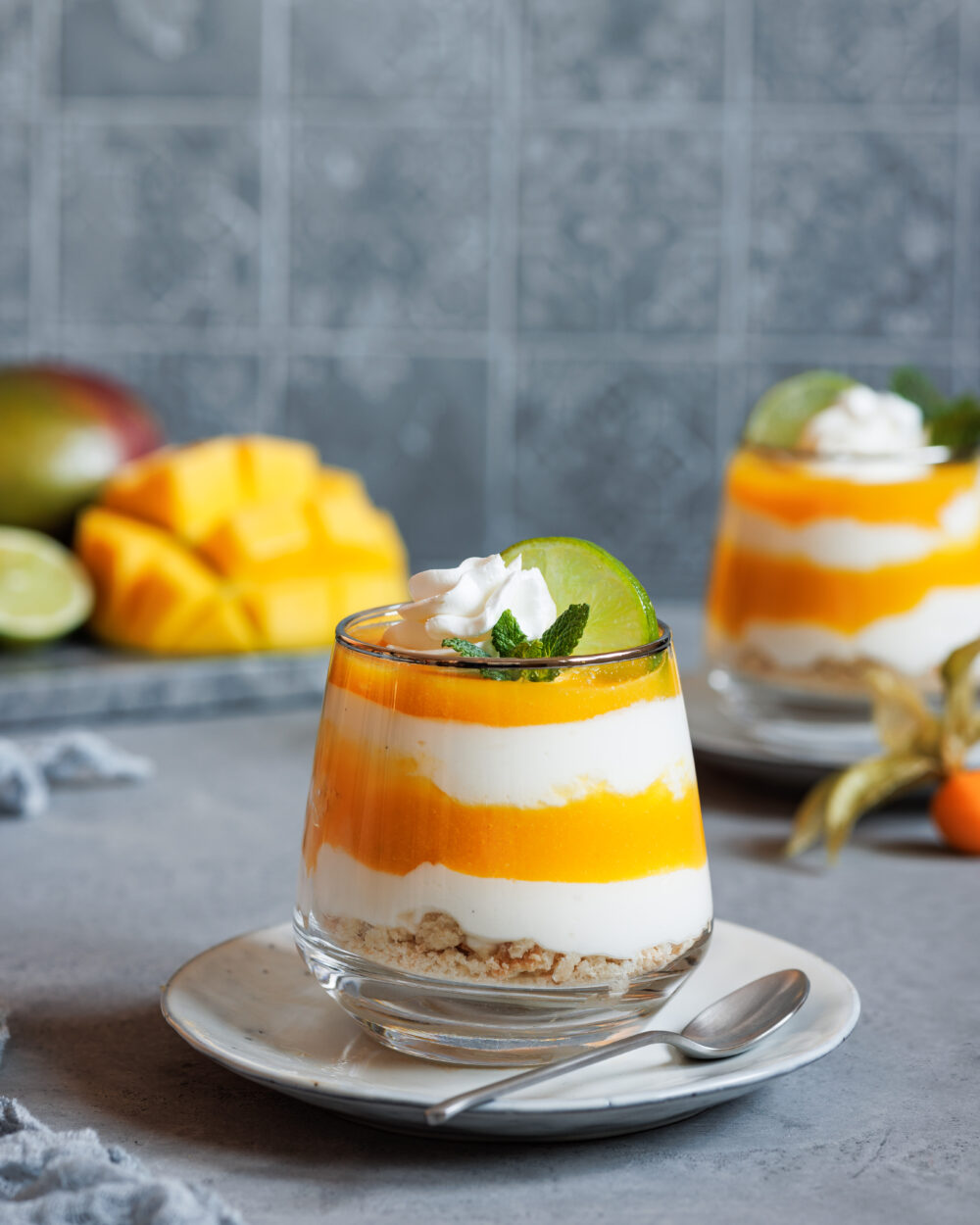Schichtdessert mit Mango und Joghurt in einem Glas mit Sahne, Minze und Limette dekoriert.
