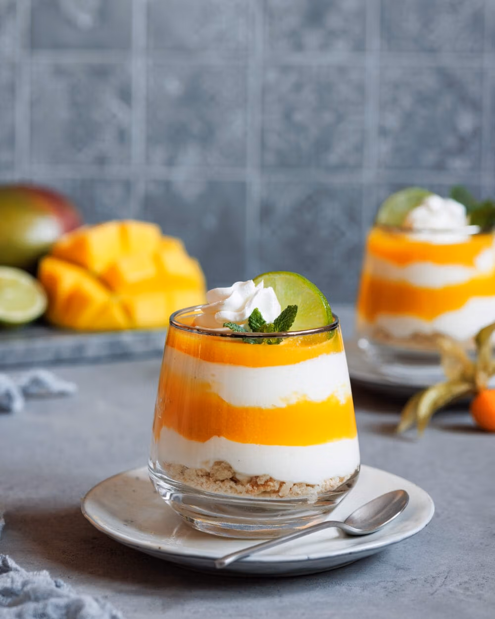 Schichtdessert mit Mango und Joghurt in einem Glas mit Sahne, Minze und Limette dekoriert.
