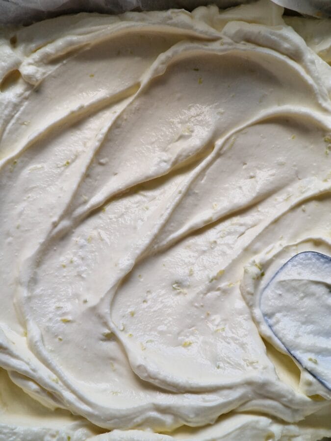 Cheesecakemasse, die mit einem Teigschaber auf dem Keksboden verteilt wird.