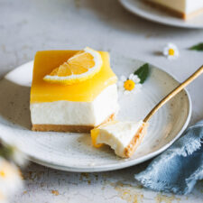 Lemon Cheesecake mit einer Kuchengabel auf einem Teller und weiteren Tellern mit Kuchen im Hintergrund.