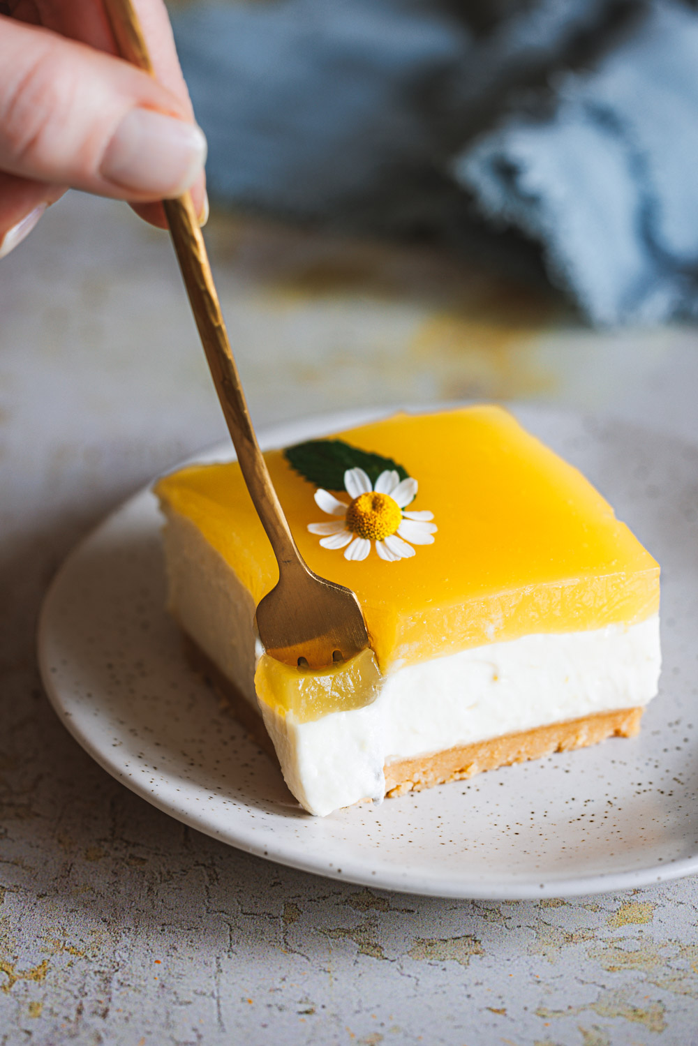 Lemon Cheesecake, ein fruchtiger Zitronen-Käsekuchen auf einem Teller mit einer Kuchengabel und weiteren Kuchenstücken im Hintergrund.