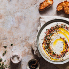 Feta-Dip in einer Schüssel mit Toppings sowie Schälchen mit Gewürzen und geröstetem Brot daneben.