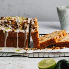 Zucchinikuchen auf einem Kuchengitter mit Zuckerguss und Limetten im Vordergrund.