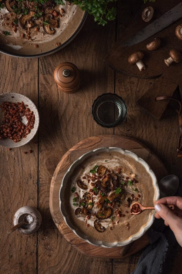 Herbstliche Pilzsuppe mit gebratenen Champignons, Speck und Petersilie.
