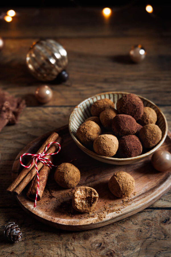 Spekulatiuskonfekt auf rustikalem Holzbrett angerichtet, dekoriert mit Zimtstangen und weihnachtlicher Beleuchtung im Hintergrund – perfekt für die Festtage.