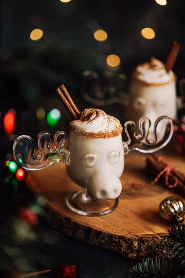 Alkoholfreier Eierpunsch in einer Elchtasse mit Sahnehaube und Zimtstange in einem weihnachtlichen Setting. 
