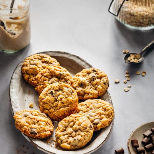 Schwedische Hafercookies mit Sauerteig auf einer rustikalen Platte, umgeben von Haferflocken, Zartbitterschokolade und einem Glas Sauerteig. Perfekt für eine süße und nachhaltige Resteverwertung.