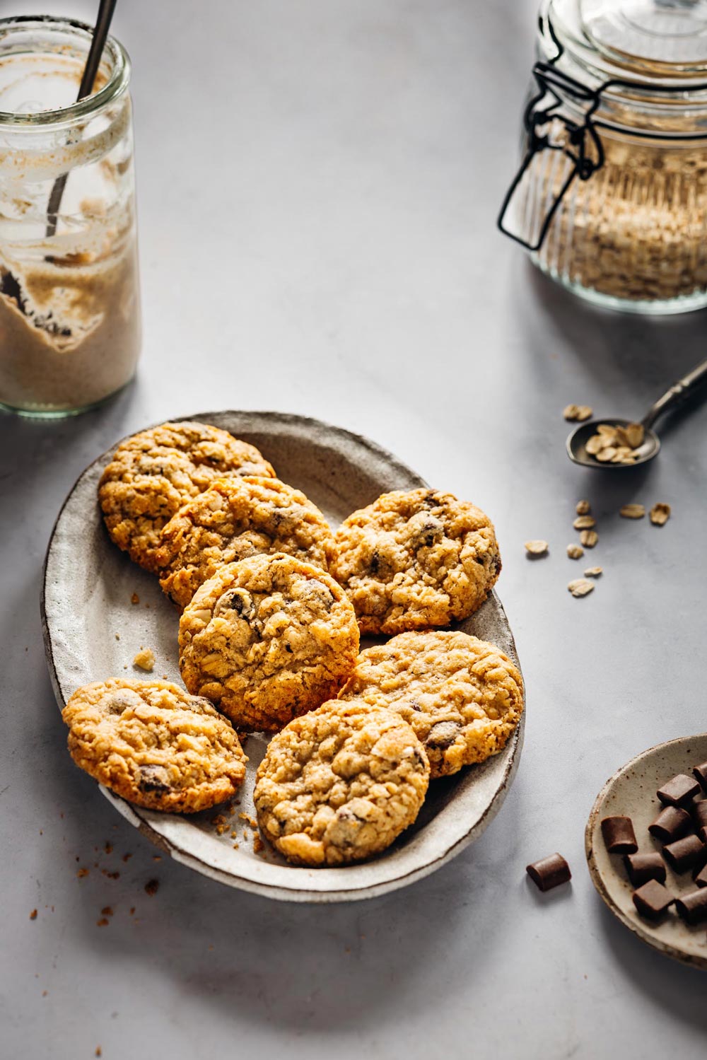 Schwedische Hafercookies mit Sauerteig auf einer rustikalen Platte, umgeben von Haferflocken, Zartbitterschokolade und einem Glas Sauerteig. Perfekt für eine süße und nachhaltige Resteverwertung.