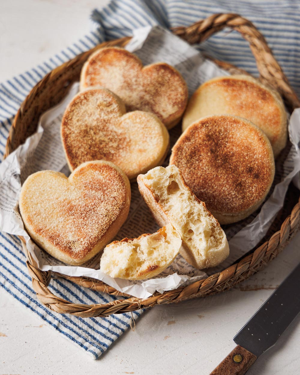 Herzförmige und runde Dinkel-Toasties in einem rustikalen Korb, serviert auf Papier und einem gestreiften Stofftuch. Ein aufgebrochenes Brötchen zeigt die weiche, luftige Krume.