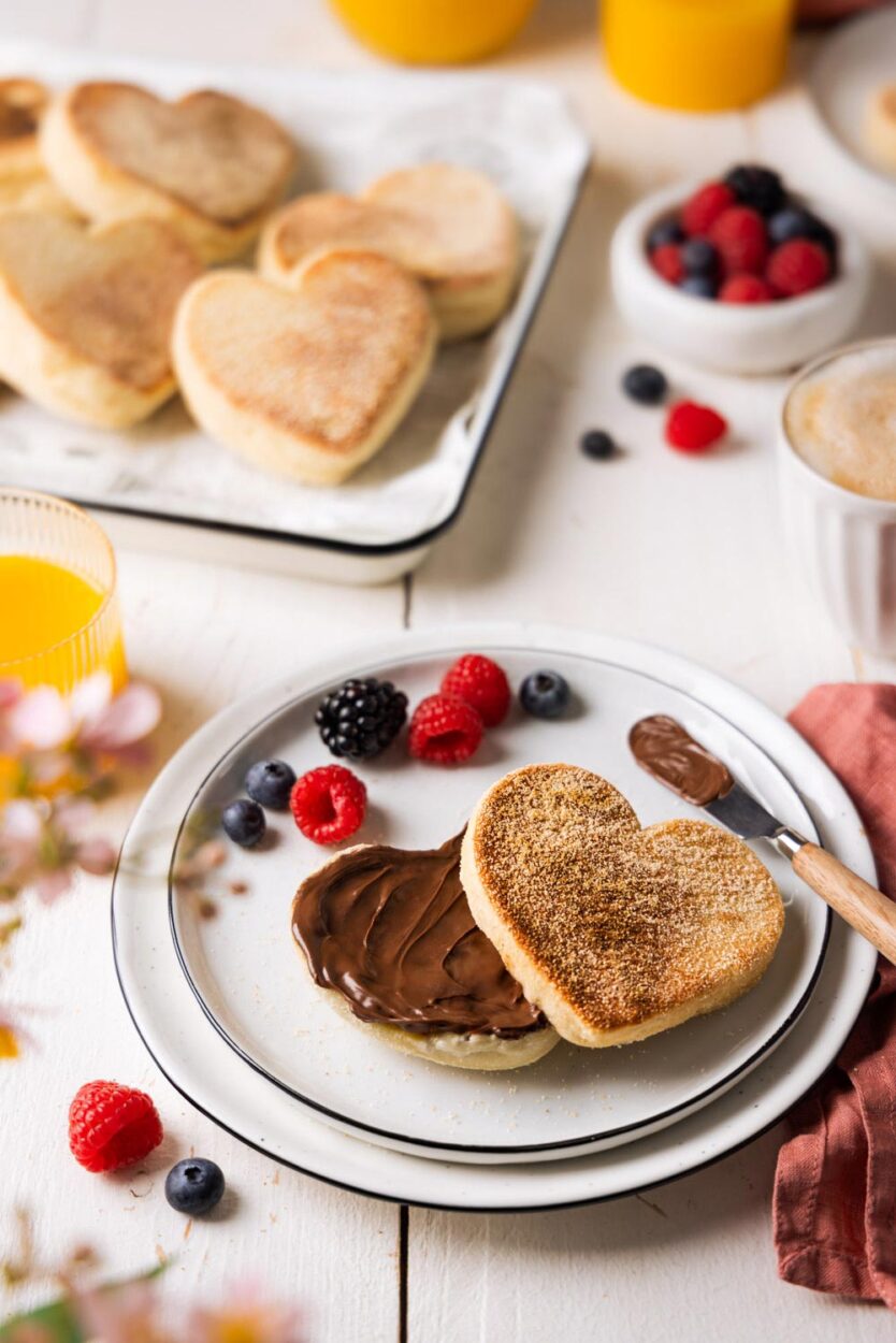 Herzförmiges Dinkel-Toasties und mit Schokoladencreme bestrichen. Umgeben von Beeren, Kaffee und Orangensaft – ein einladendes Frühstückssetting für besondere Anlässe.