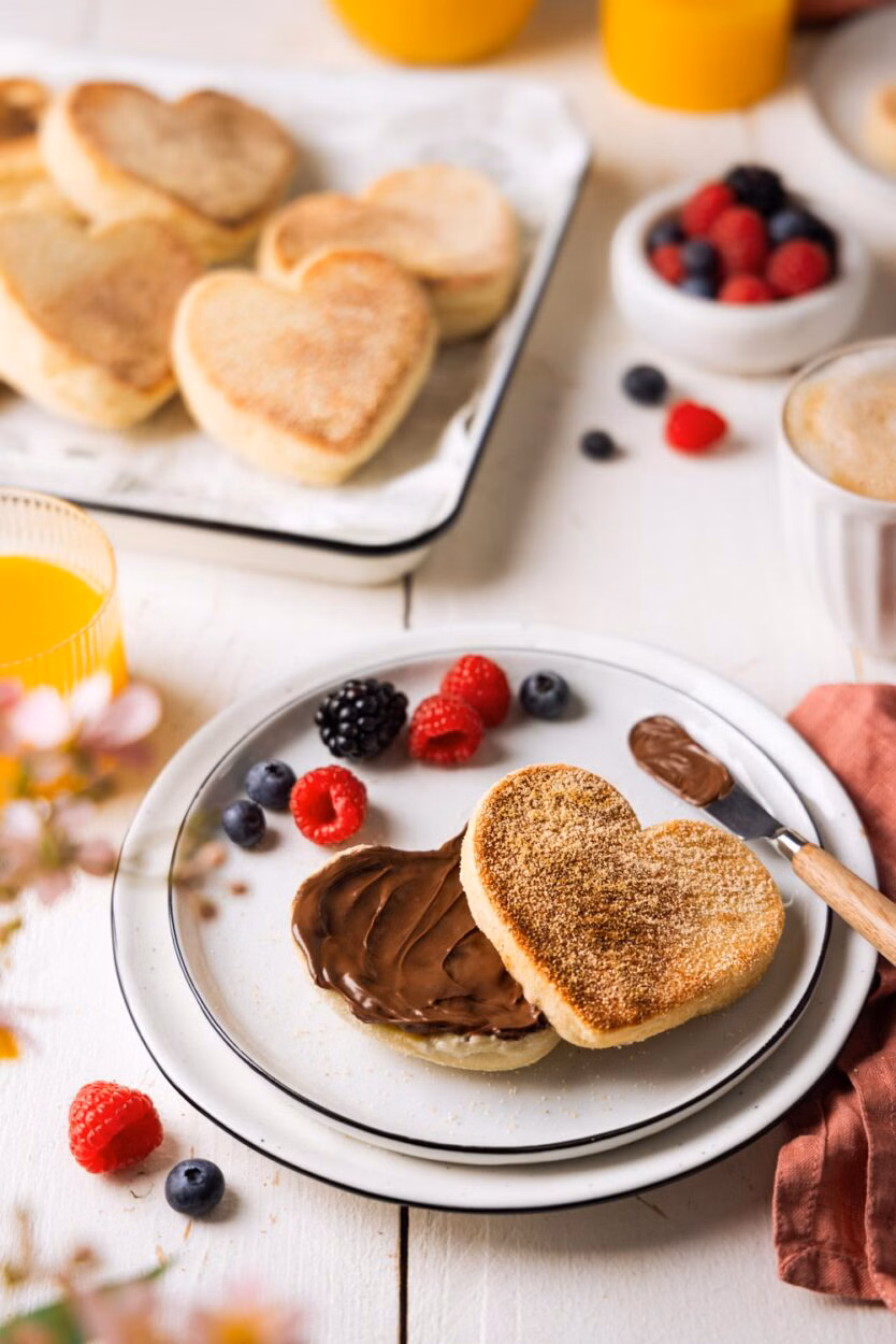 Herzförmiges Dinkel-Toasties und mit Schokoladencreme bestrichen. Umgeben von Beeren, Kaffee und Orangensaft – ein einladendes Frühstückssetting für besondere Anlässe.