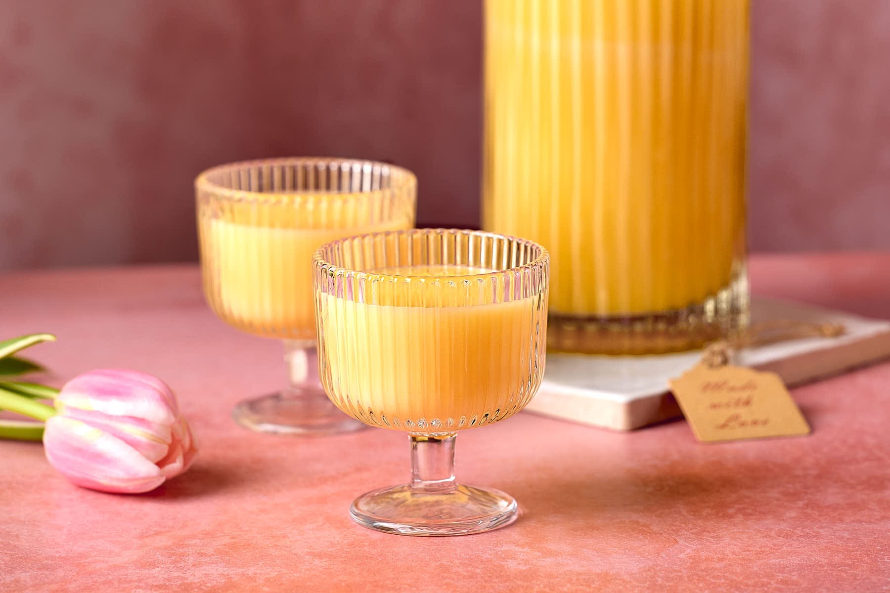 Eine Flasche mit gelbem Eierlikör und zwei gefüllte Gläser, dekoriert mit rosafarbenen Tulpen.