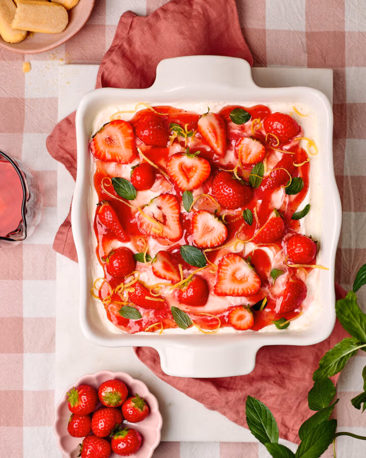 Erdbeer-Tiramisu in einer Keramikform mit dem Löffelbiskuit und Erdbeeren daneben.