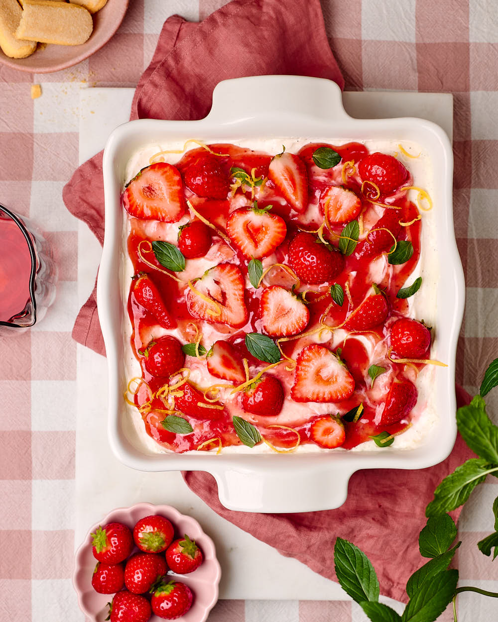Erdbeer-Tiramisu in einer Keramikform mit dem Löffelbiskuit und Erdbeeren daneben.