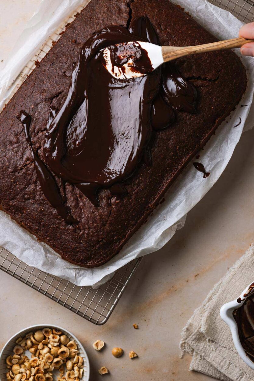 Schokoladen-Ganache wird auf einen Zucchinikuchen vom Blech aufgetragen.