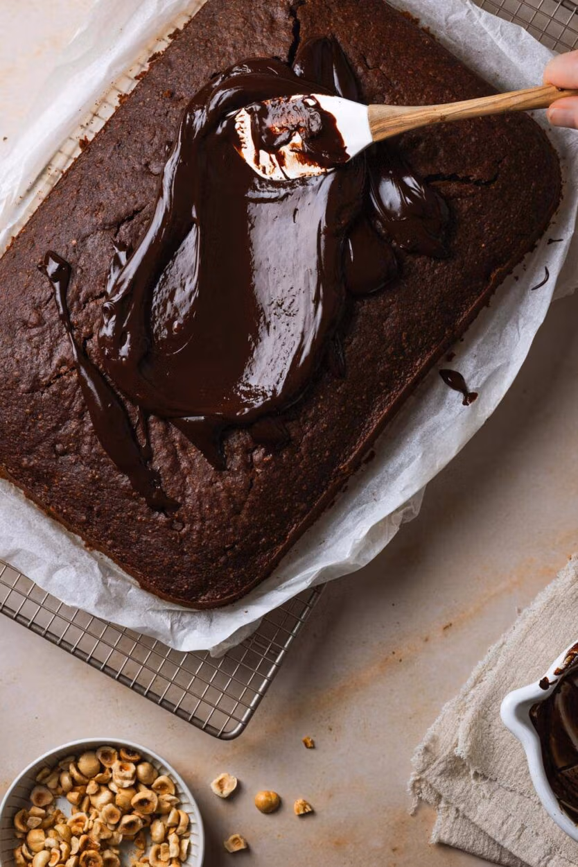 Schokoladen-Ganache wird auf einen Zucchinikuchen vom Blech aufgetragen.