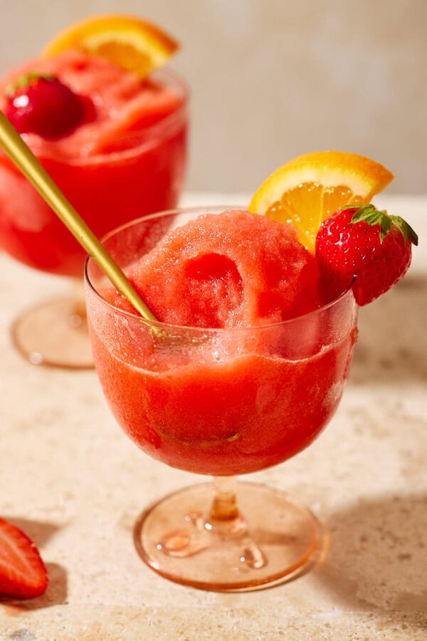 Detailaufnahme: Goldener Löffel steckt im cremigen Aperol-Erdbeer-Sorbet, garniert mit Orange und Erdbeere.