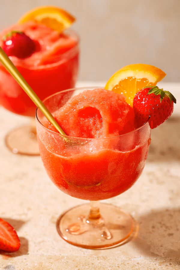 Detailaufnahme: Goldener Löffel steckt im cremigen Aperol-Erdbeer-Sorbet, garniert mit Orange und Erdbeere.