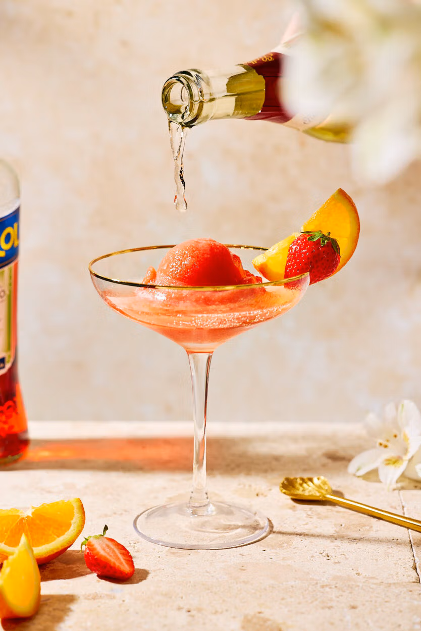 Frozen Aperol Spritz in Cocktailglas wird mit Sekt oder Prosecco aufgegossen – perfekt für heiße Sommertage.