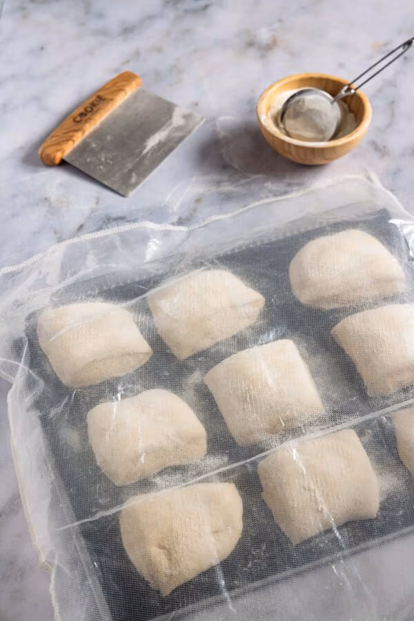 Stückgare von Brötchenteiglinge auf einem Backblech – besonders bei der Übernachtgare sollten diese gut abgedeckt sein. 