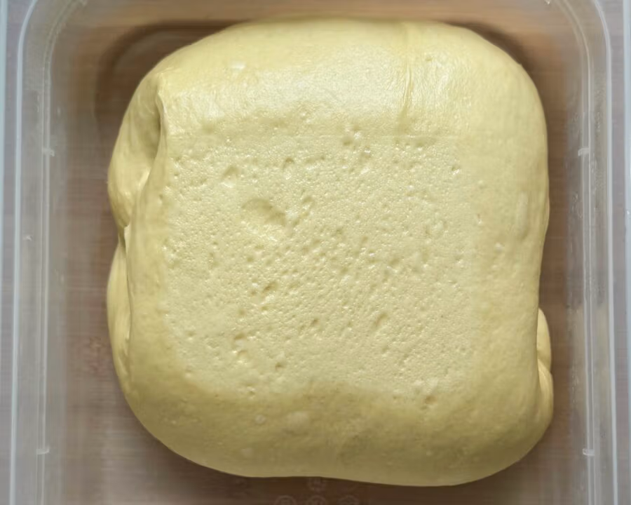 Reifer zuvor gefalteter Teig für Brioche Burger Buns in einer Teigwanne.