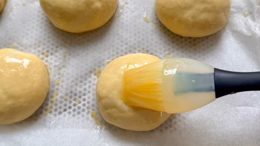 Teiglinge für Brioche Buns werden mit Eistreiche eingestrichen.