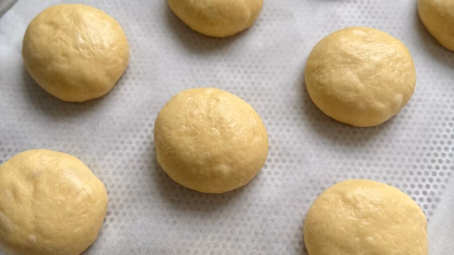 Geformete Teiglinge für Brioche Buns auf einem mit Backpapier belegtem Backblech.