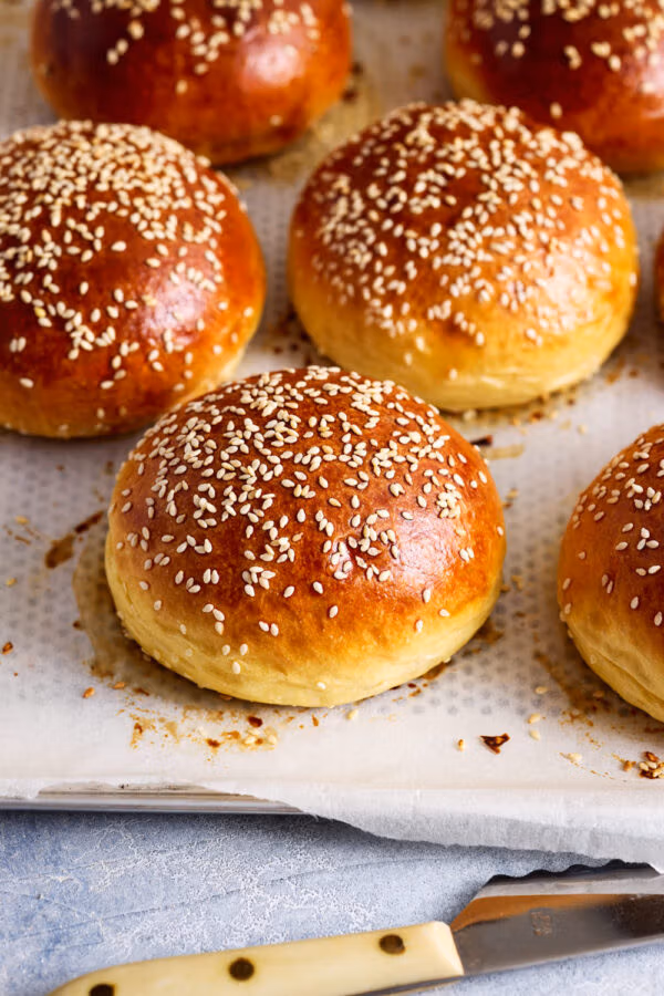 Mehrere Brioche Burger Buns auf einem mit Backpapier belegten Backblech, goldbraun gebacken.