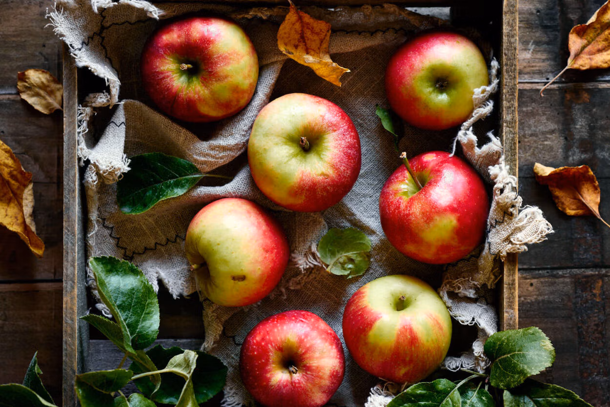 Äpfel auf einem rustikalen Leinentuch in einer Holzkiste.