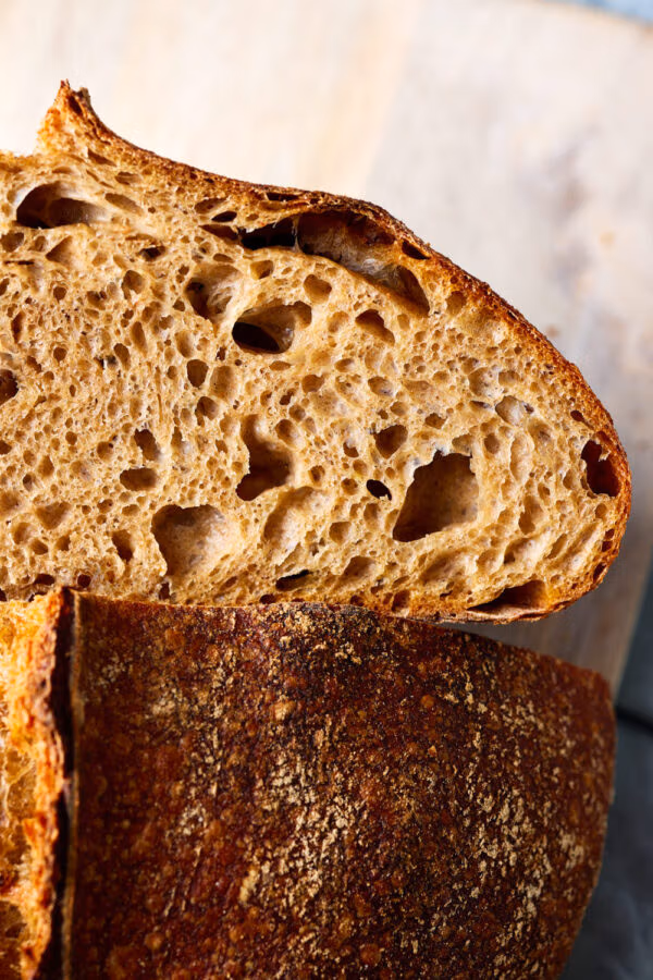 Dinkel-Sauerteigbrot aufgeschnitten auf einem Holzbrett mit Nahaufnahme einer sichtbaren lockeren Krume.