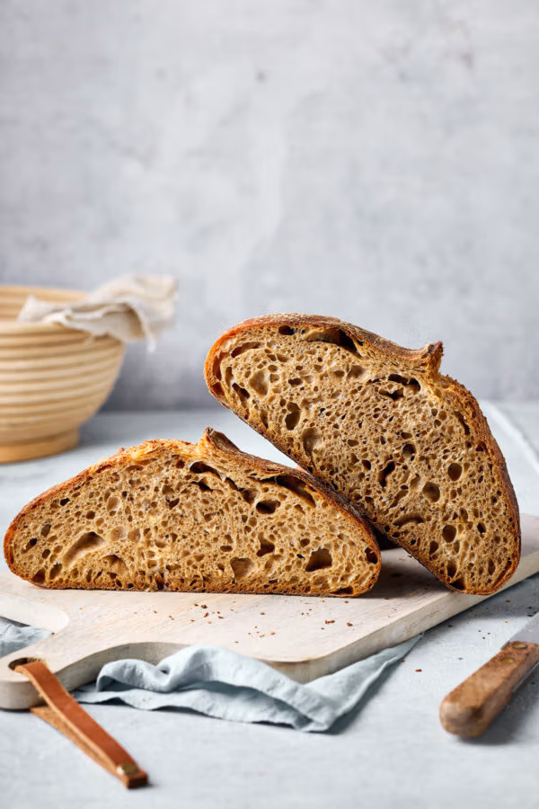 Dinkel-Sauerteigbrot aufgeschnitten auf einem Holzbrett mit sichtbarer lockerer Krume.